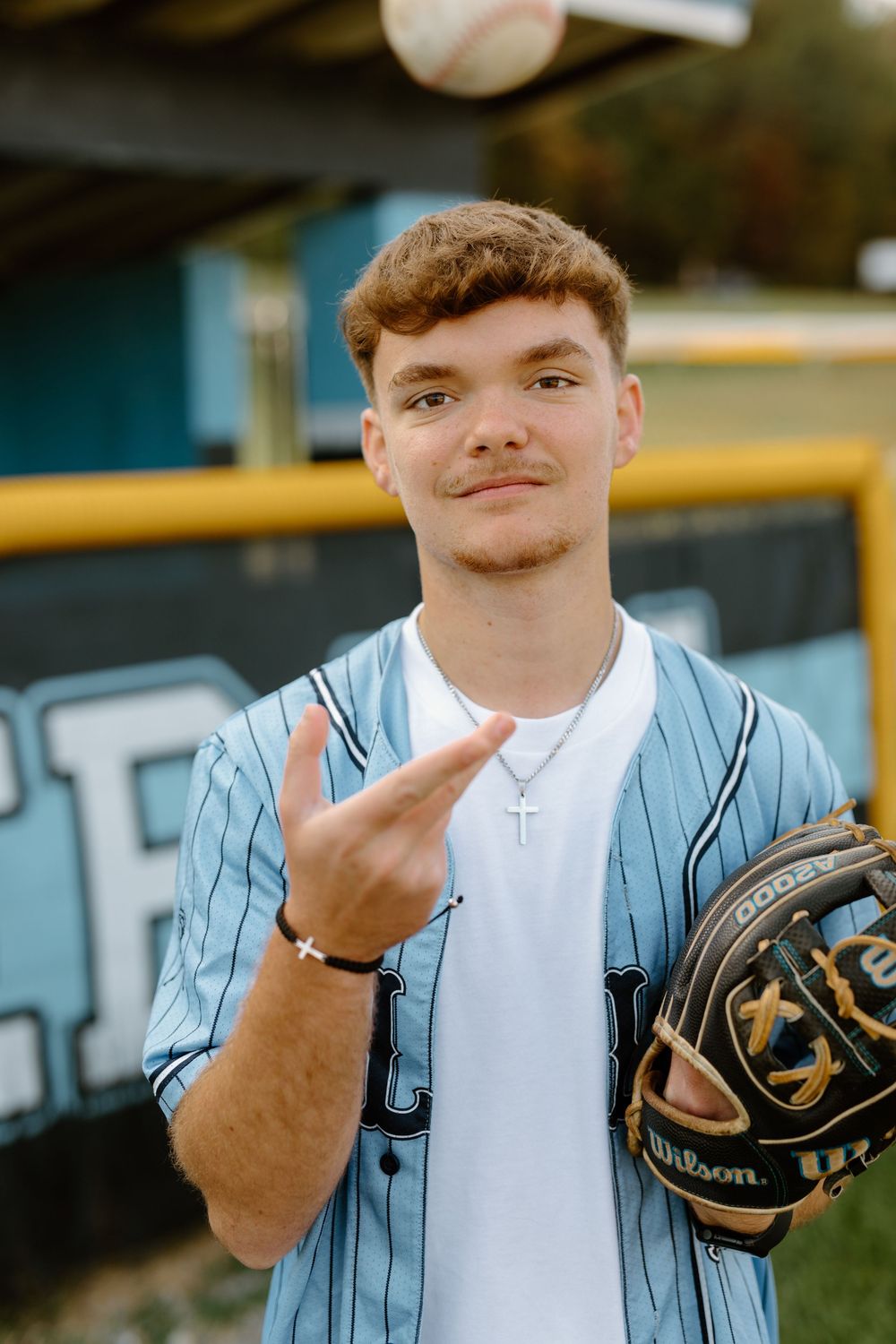 Baseball player in blue pinstripe jersey holding Wilson glove and making peace sign.