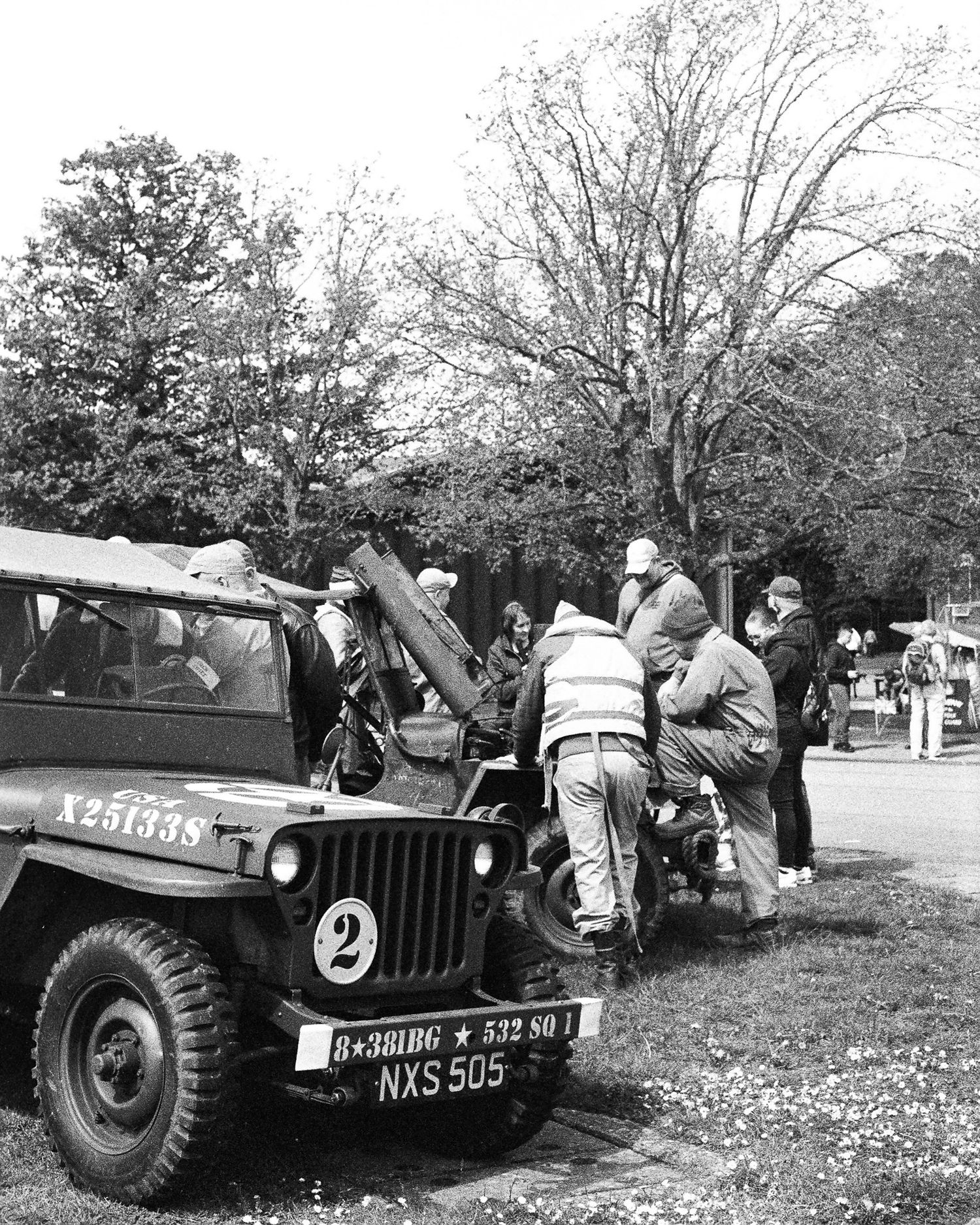 Black and white photo of a military Jeep with license plate NXS 505 surrounded by people in a park setting.