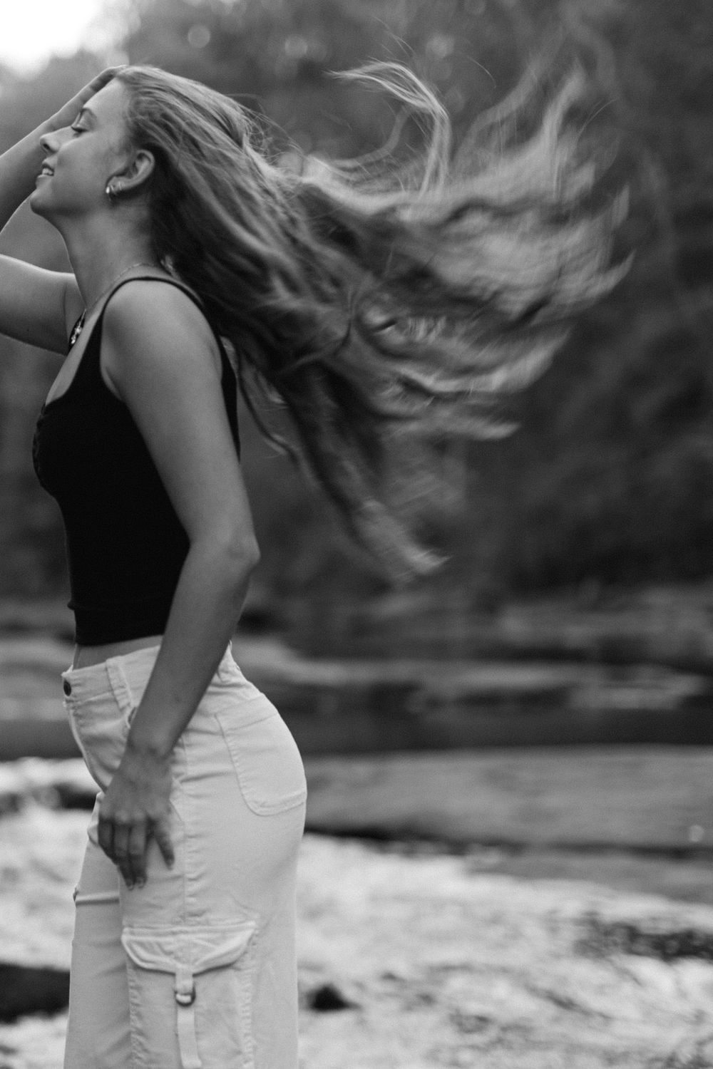 Black and white dramatic shot of young woman tossing long hair near a flowing river outdoors.