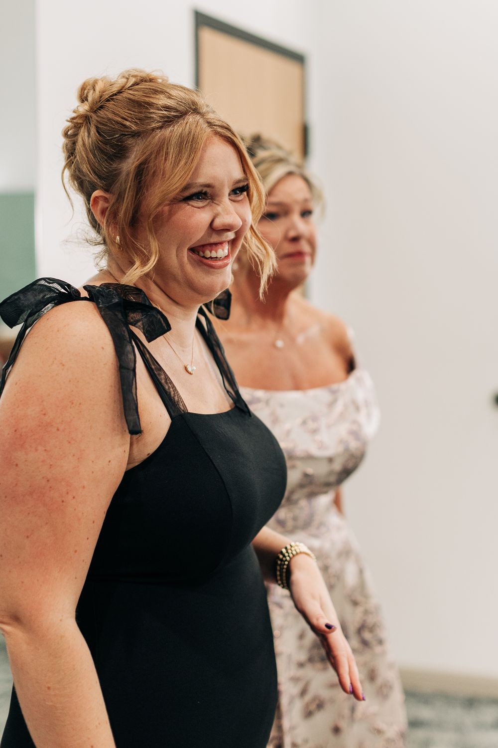 Smiling bridesmaid in black dress with bow shoulders laughing at a wedding celebration.