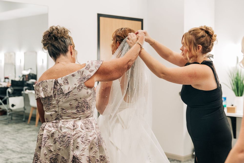 Two women helping a bride adjust her veil in a bridal suite before her wedding ceremony.
