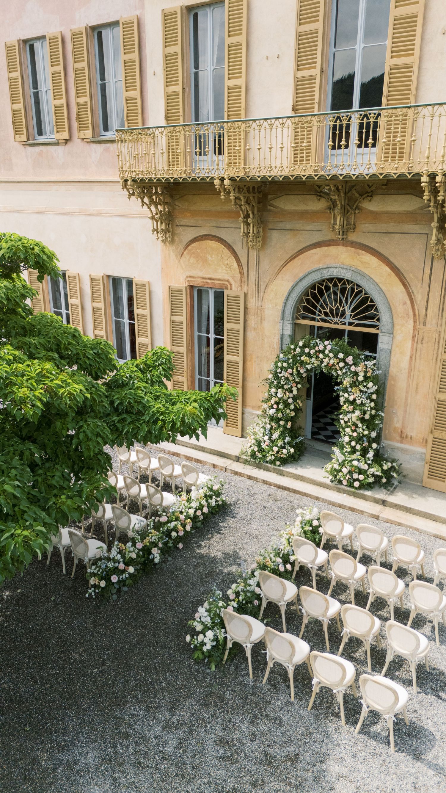 Elegant outdoor wedding ceremony setup with white chairs and floral arch at a classic Italian villa.