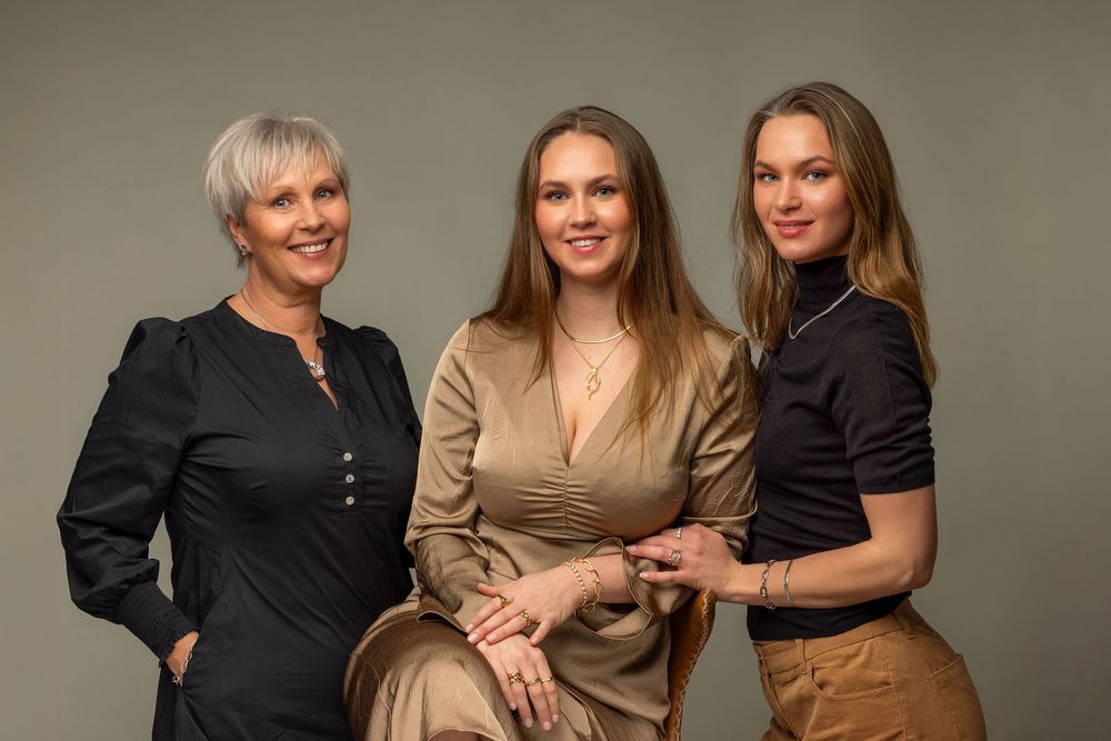 Three elegant women posing together for a professional studio portrait against a gray background.