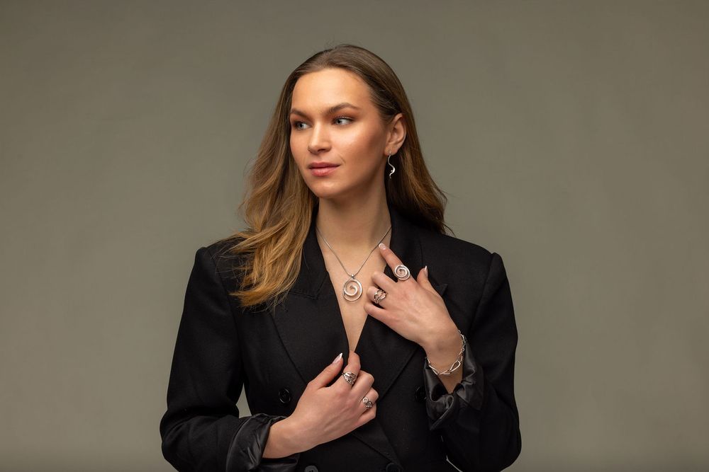 Woman modeling silver necklace and bracelet in black blazer against gray background.