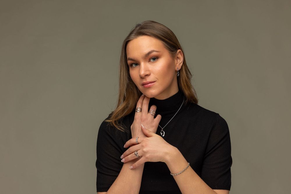Young woman in black turtleneck poses gracefully against gray background, wearing delicate jewelry.