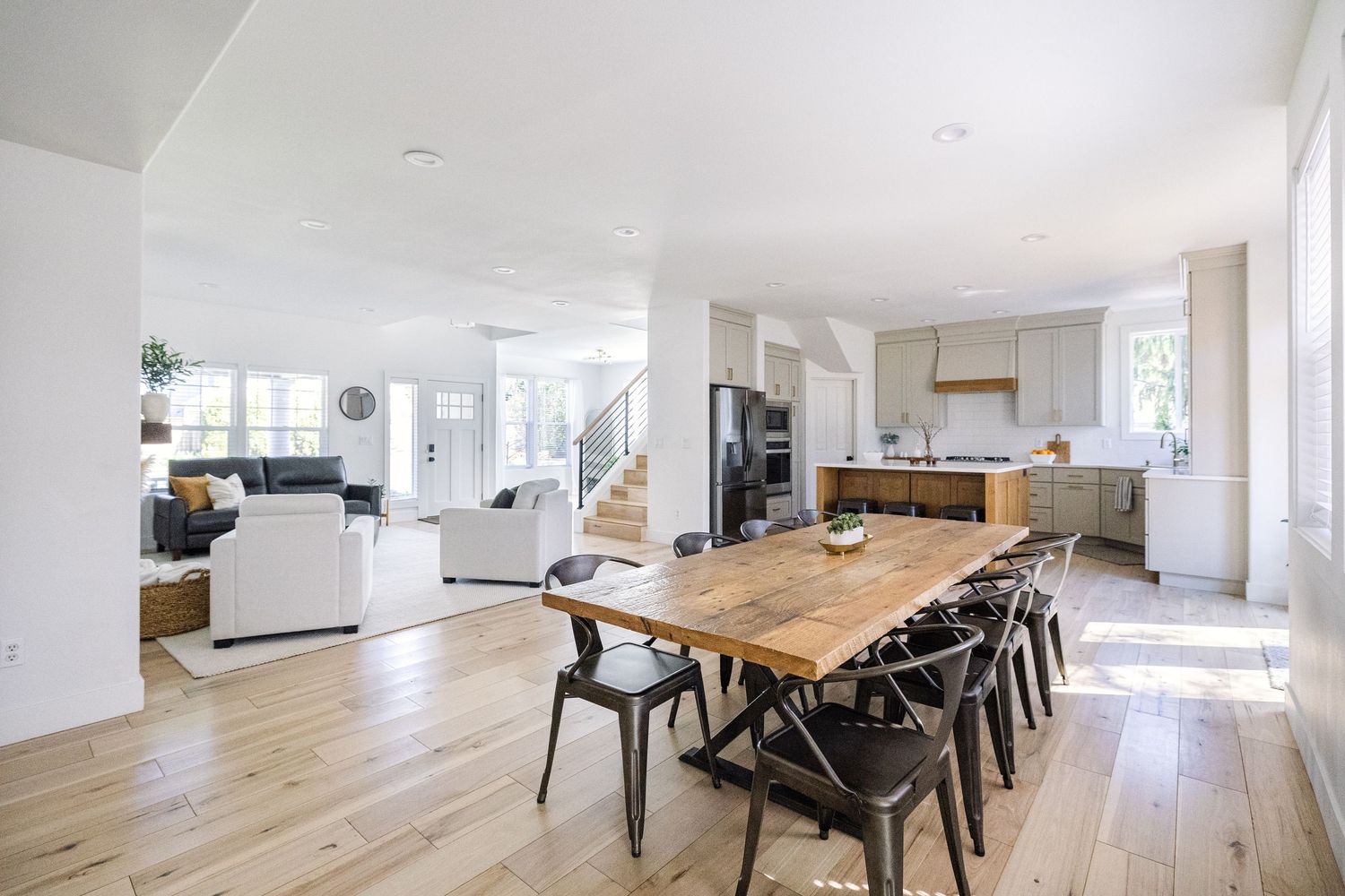 Bright open-concept dining and kitchen area featuring a rustic wood table, modern chairs, and light hardwood floors.