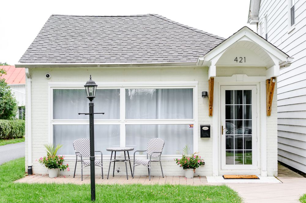 White cottage exterior at 421 featuring outdoor seating, large windows, black lamp post, and lush green lawn.