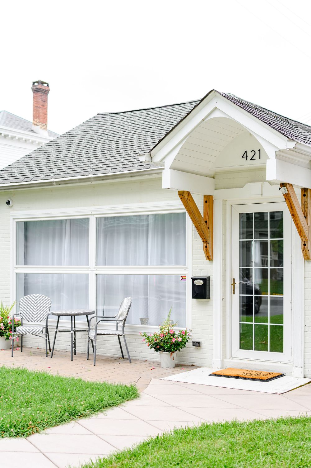 Charming white cottage at 421 with a covered entryway, patio seating, and lush green lawn.