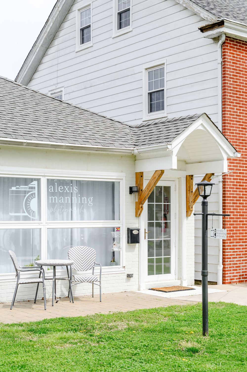 Alexis Manning salon exterior with white siding, brick accents, French doors, outdoor seating, and manicured lawn.