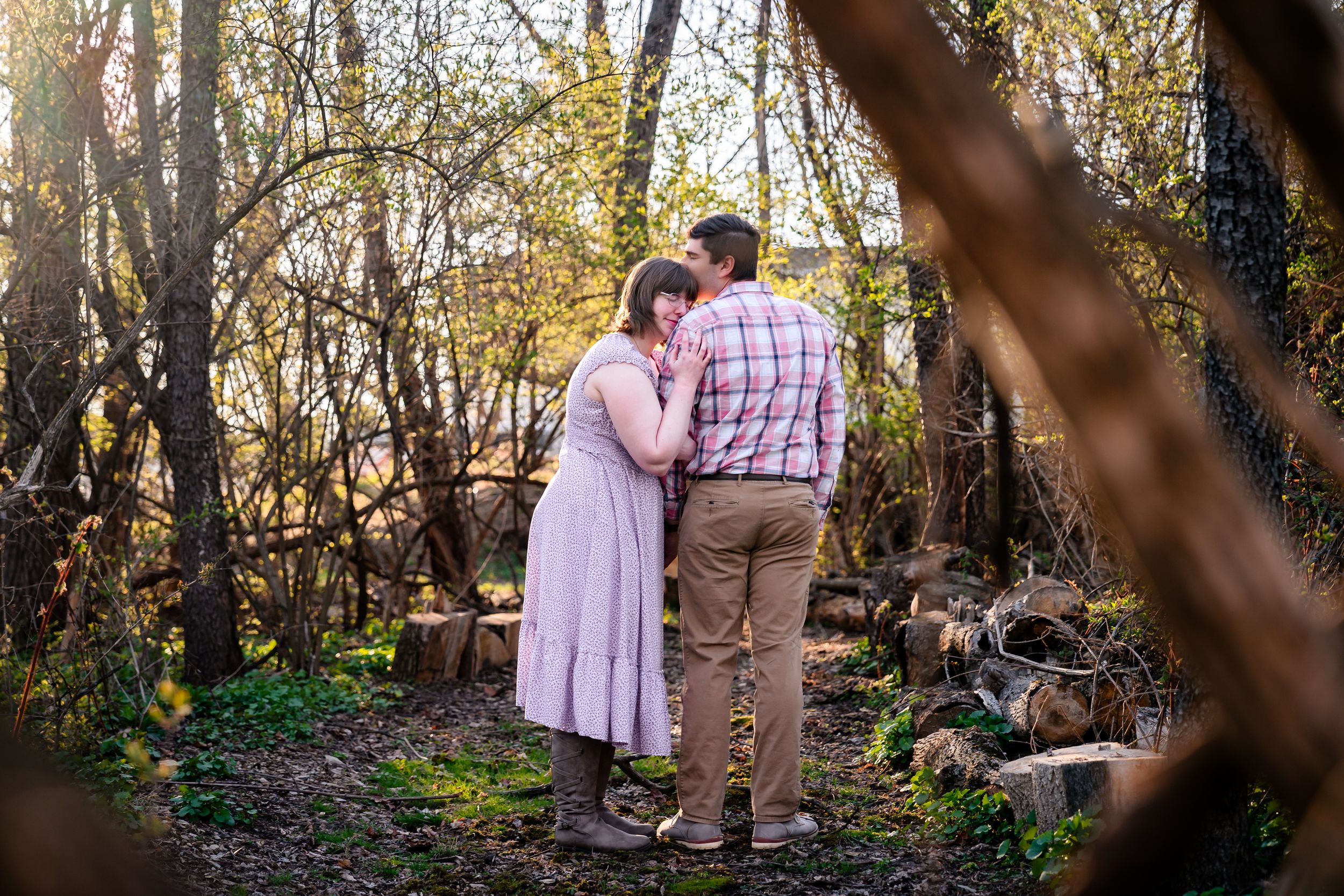 Romantic couple shares a tender moment embracing in a sunlit woodland setting.