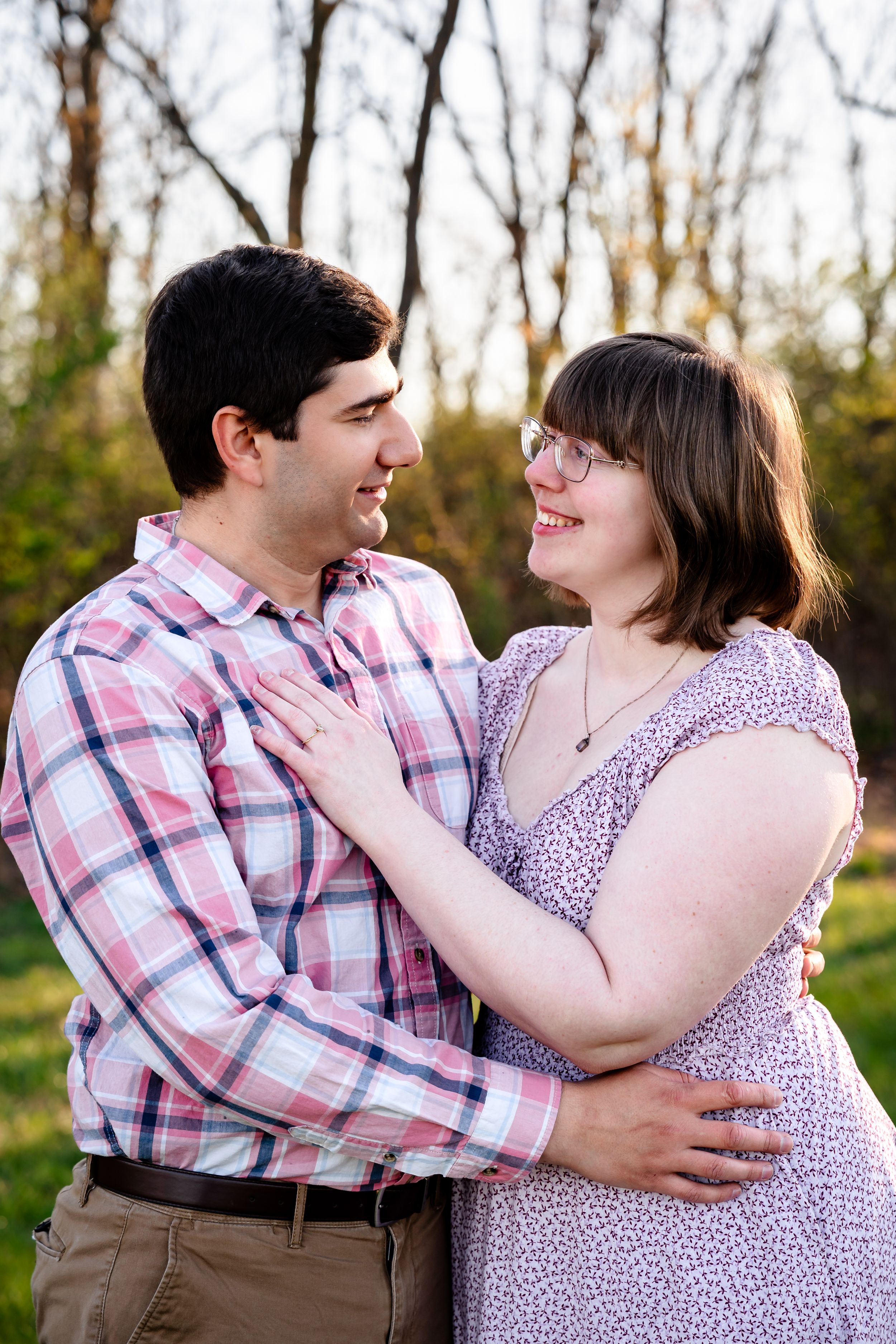 Couple embracing and smiling at each other outdoors in a park during golden hour.