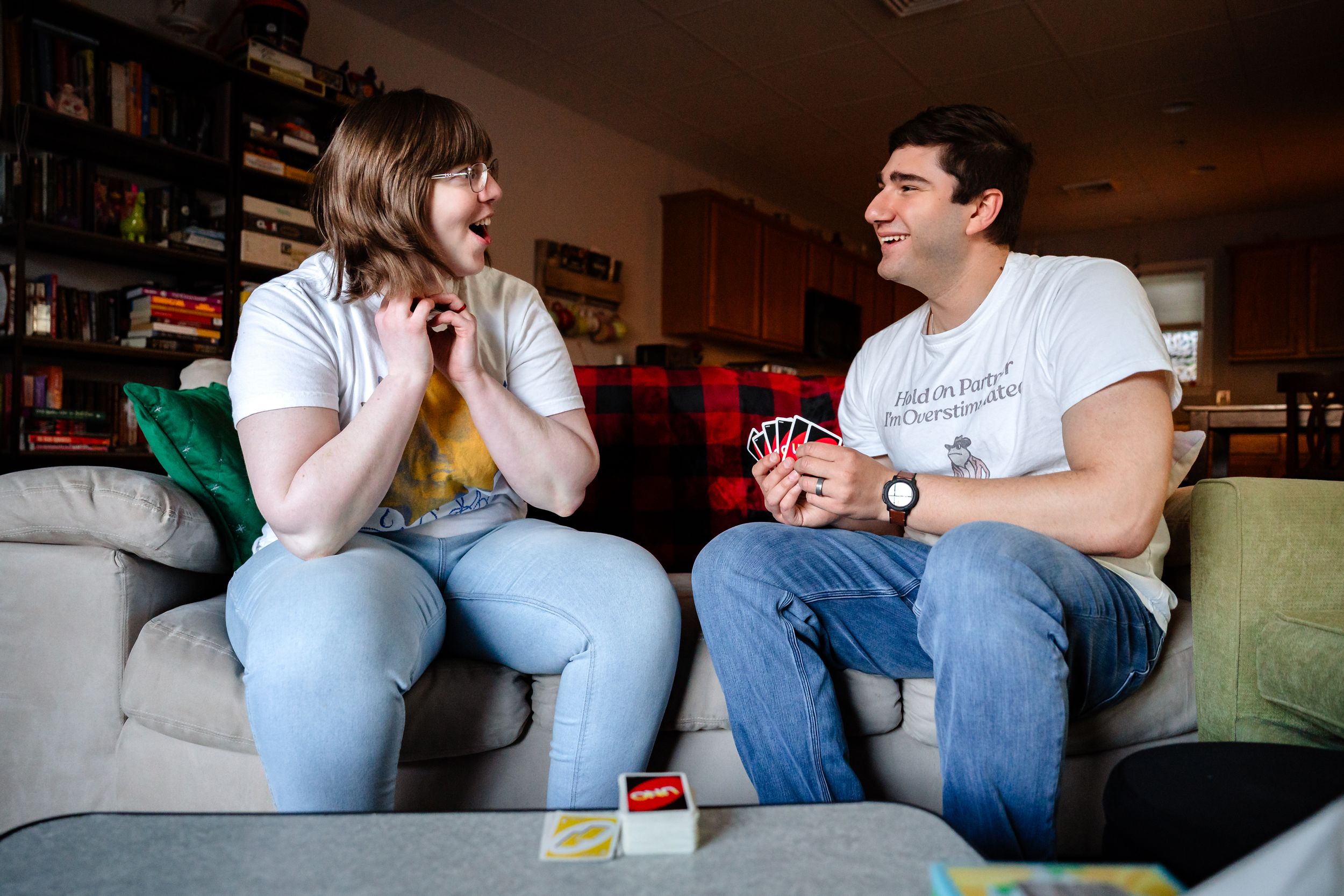 Man and woman laughing while playing Uno card game on a couch indoors.