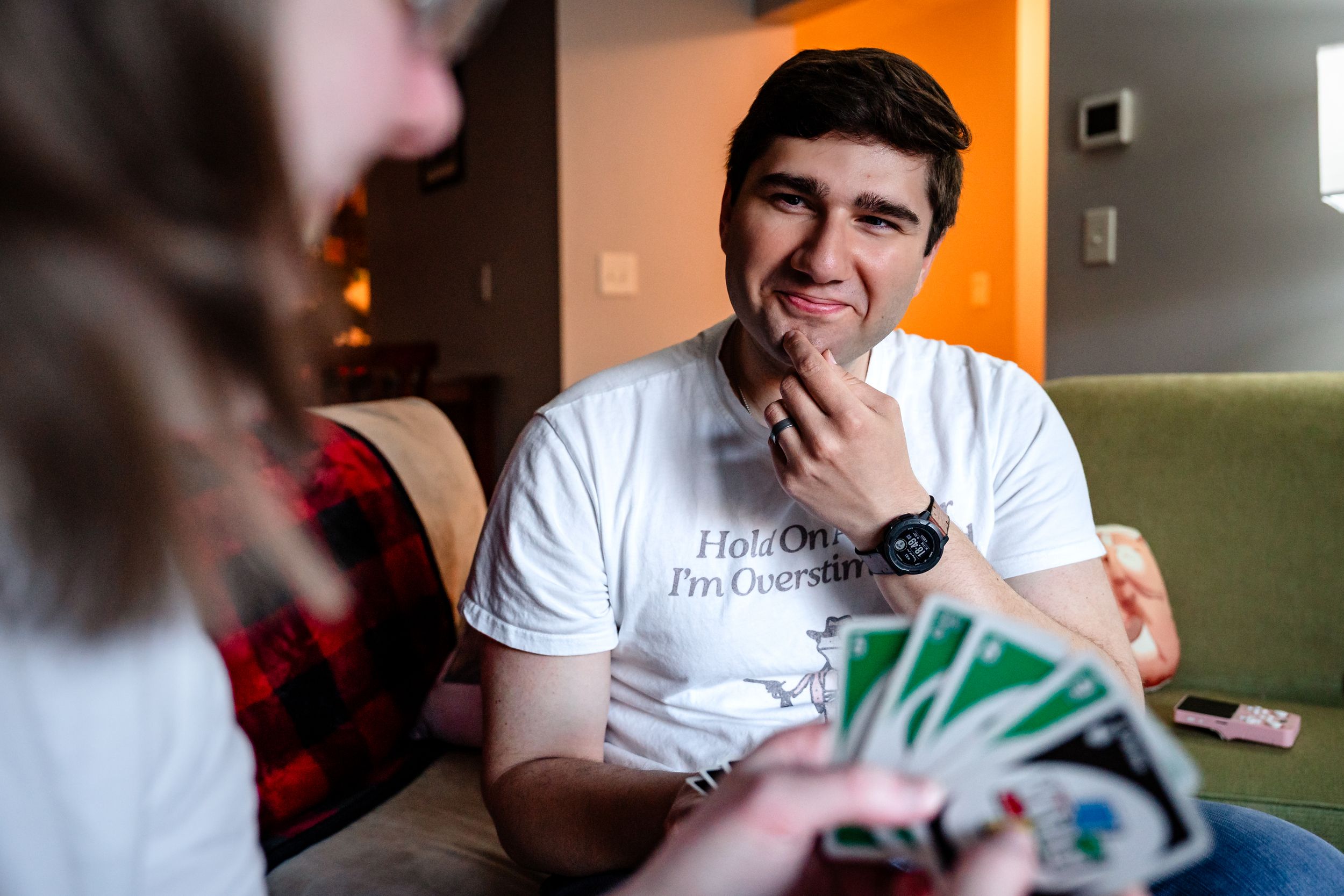 Young man smiling while playing Uno card game indoors wearing a white graphic t-shirt.