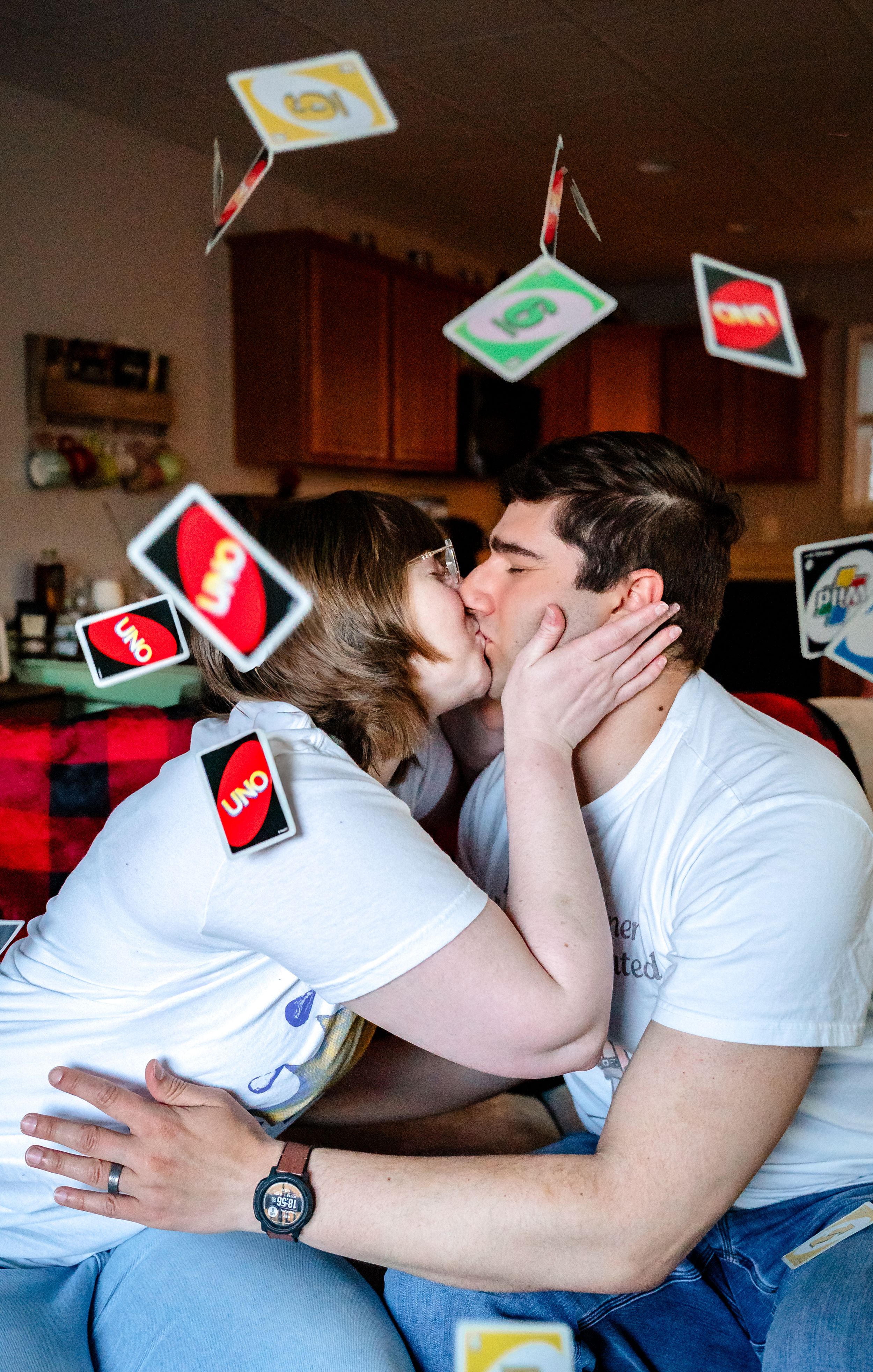 Couple kissing with Uno cards flying through the air around them indoors.