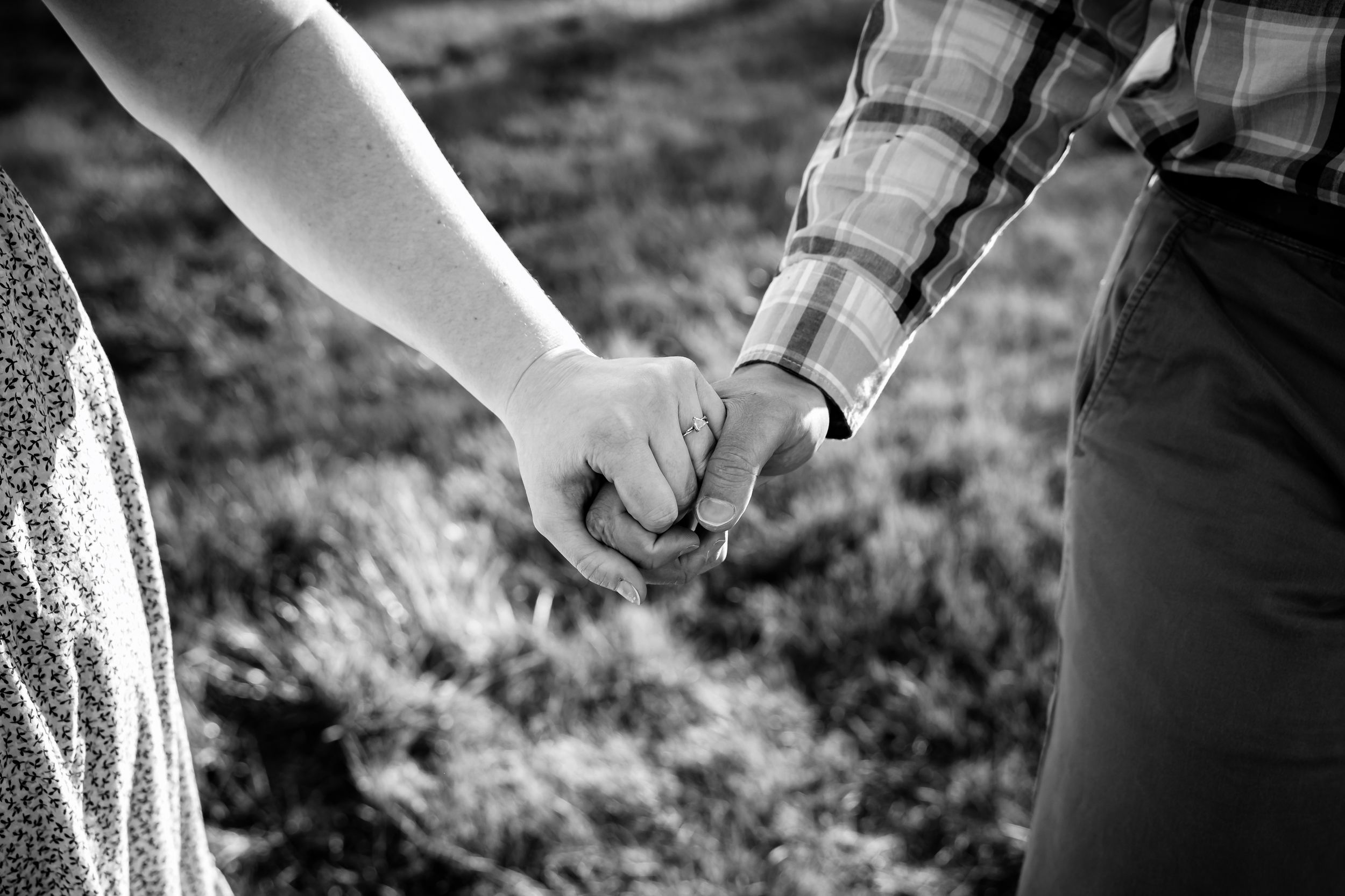 Black and white photo of a couple holding hands outdoors, wearing casual clothes, standing on grass.