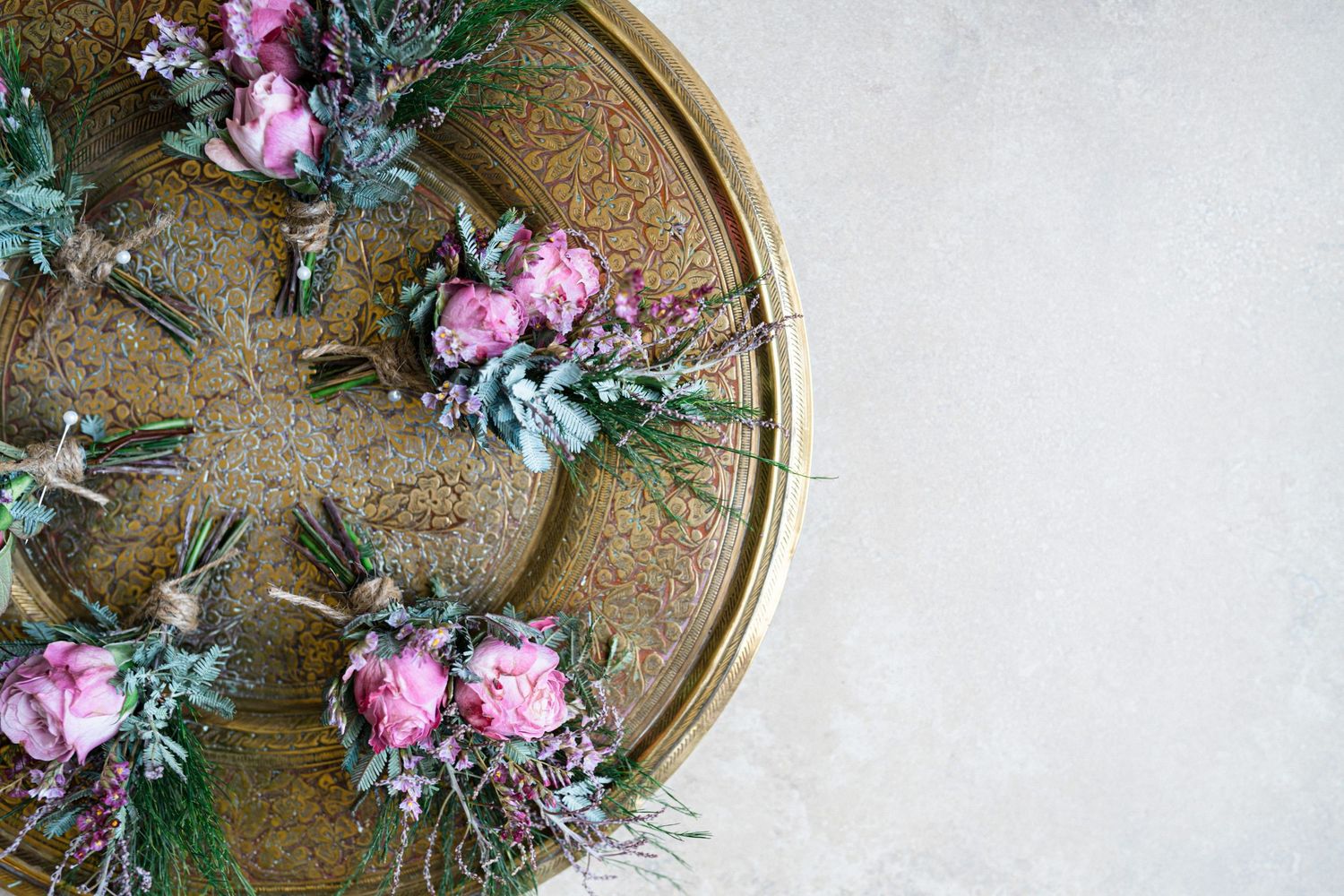 Pink floral boutonnieres with greenery arranged on a gold circular tray against a light background.