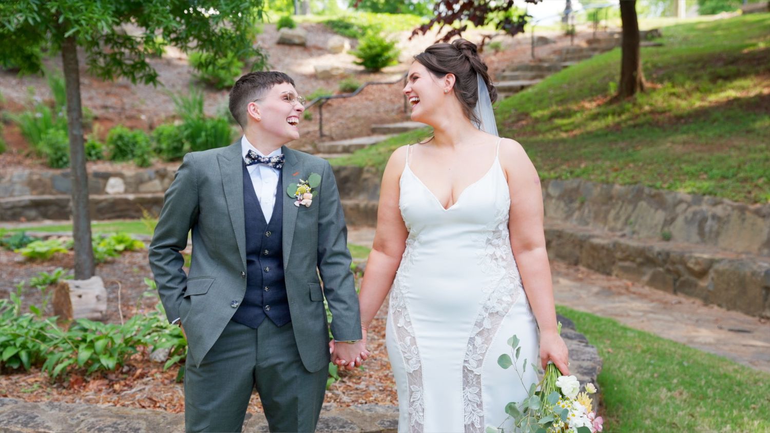 A couple in wedding attire walking on a garden path, sharing a joyful moment together on their special day.