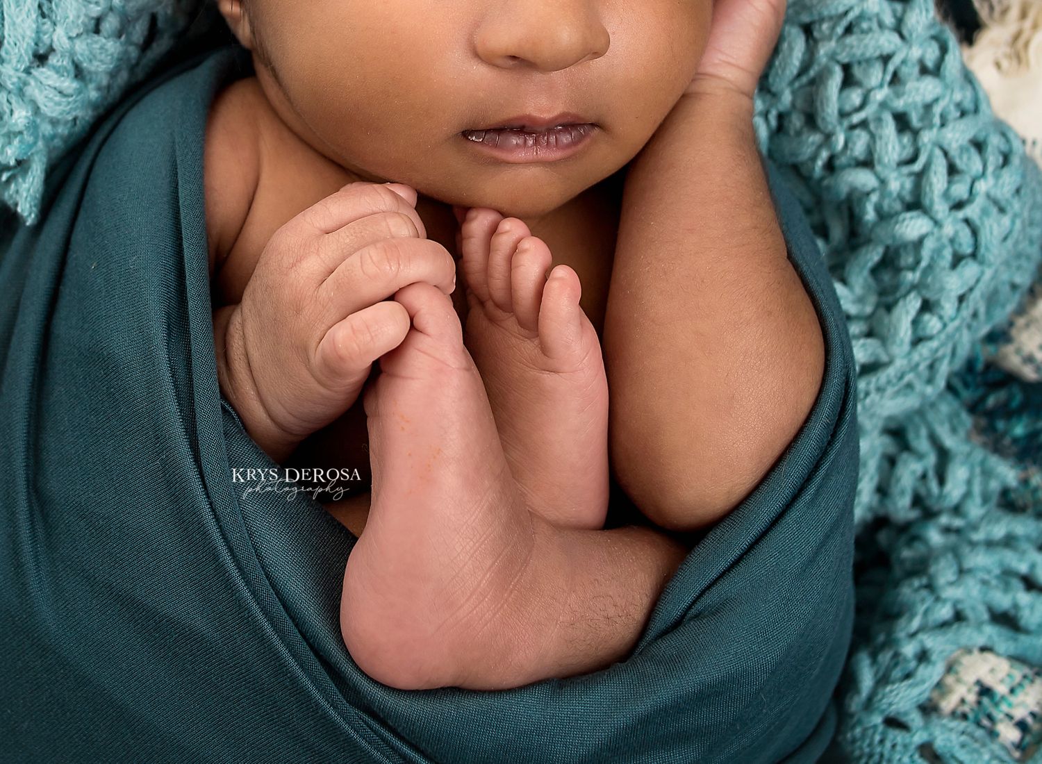 Close-up of baby wrapped in teal fabric with tiny fingers curled near face.