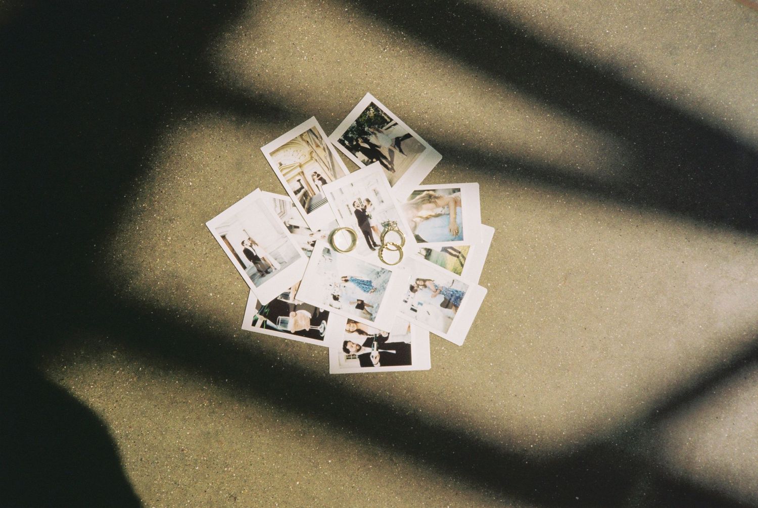 Scattered Polaroid photos arranged in a circle on a beige floor with dramatic shadows creating an artistic flat lay composition.