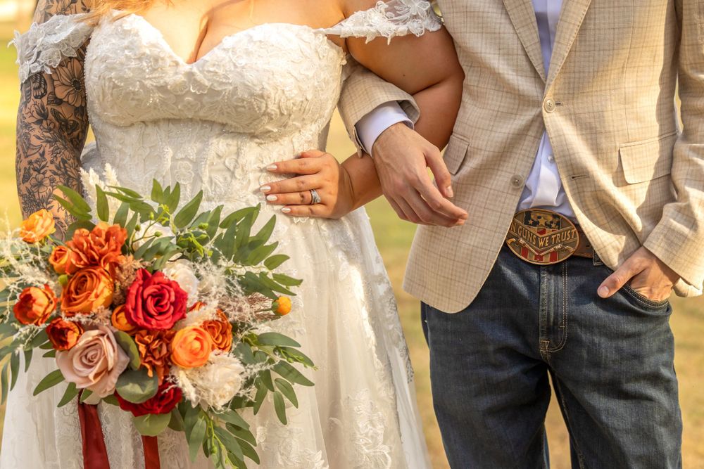 Beautiful autumn wedding bouquet with orange and red flowers next to couple in dress and tan suit jacket taken by fresno photographer.