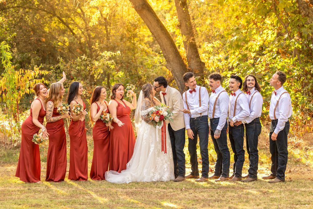 Wedding party in burgundy dresses and suspenders pose together in golden sunlit forest setting taken by fresno photographer.