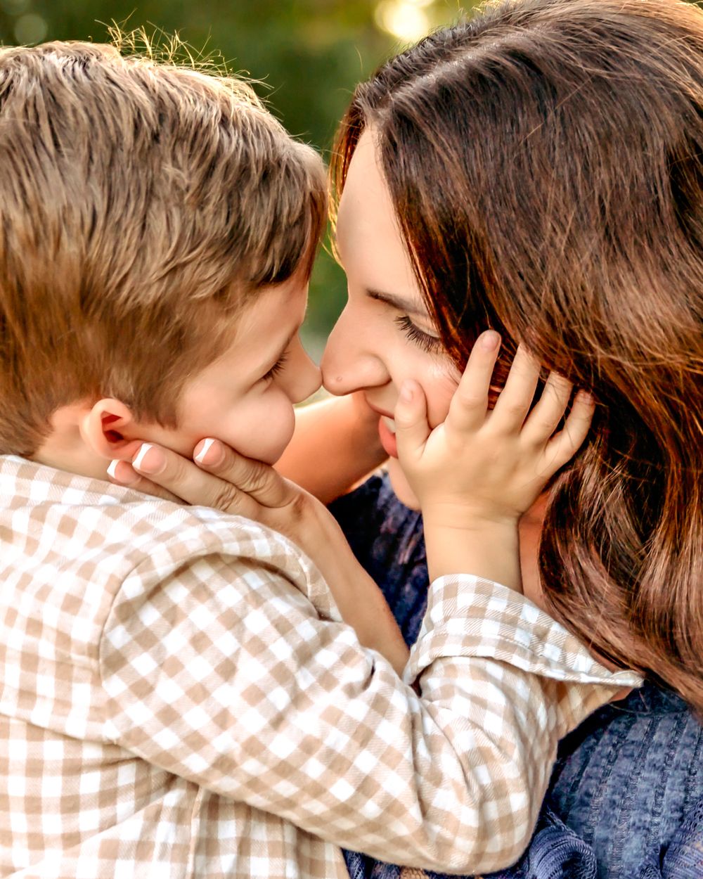 A tender moment between parent and child sharing an intimate nose-to-nose touch while outdoors in natural light taken by local photographer.