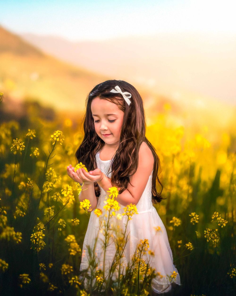 A child in a white dress explores a vibrant field of yellow canola flowers at golden hour taken by local photographer in Fresno,ca.