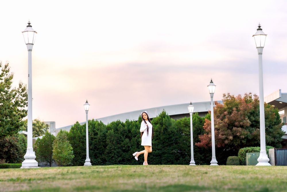 New nursing grad jumps playfully between decorative white light posts in a park at sunset taken by local photographer in Fresno,ca