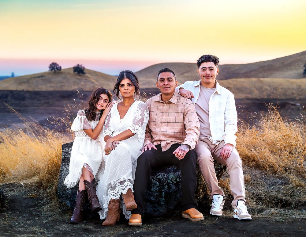 Family of four poses on hillside at sunset wearing white and neutral outfits in golden light taken by local photographer in Fresno,ca.