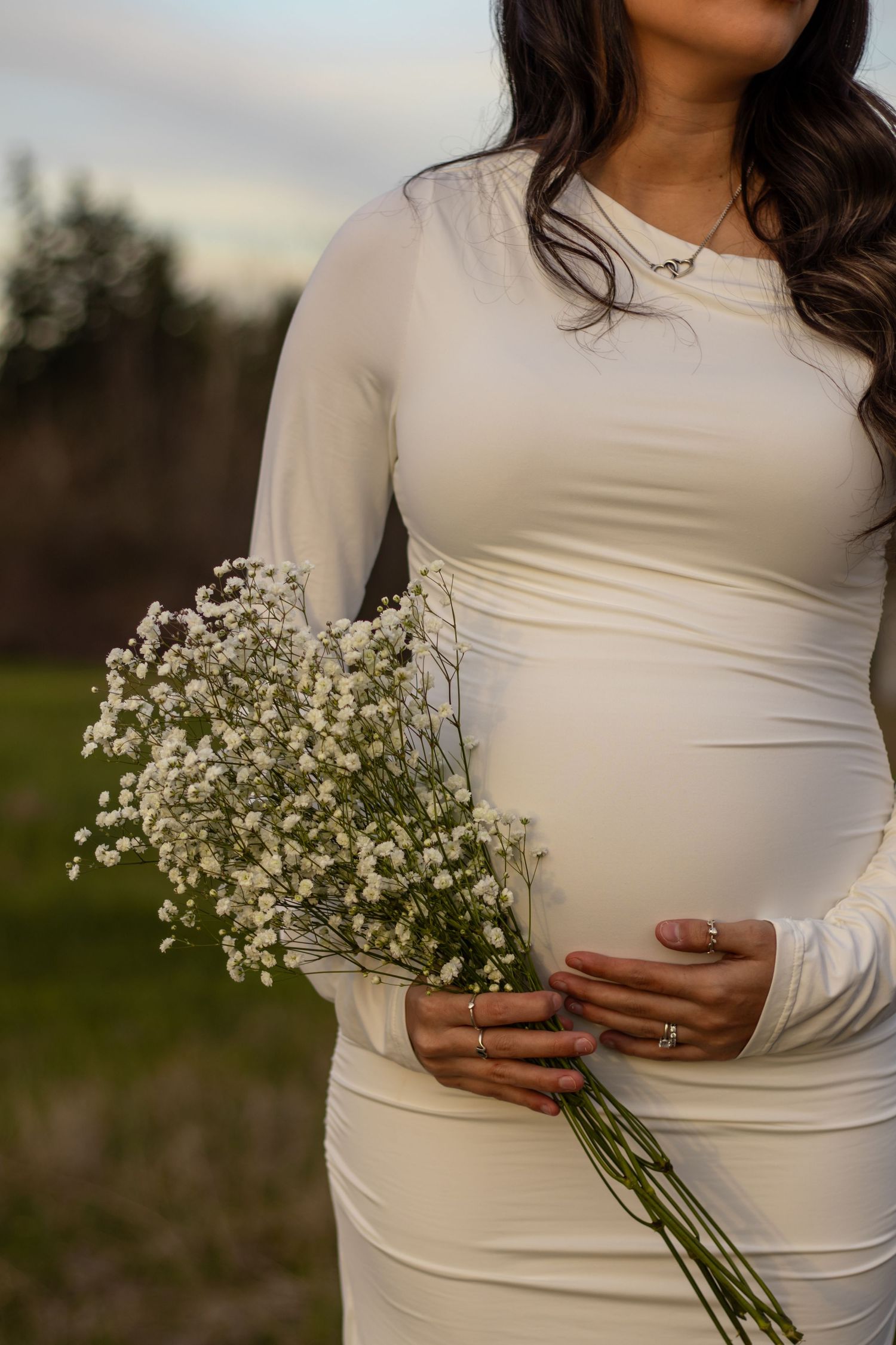 Pregnant woman in white fitted dress holding white flower bouquet outdoors at dusk in eatonville washington captured by roy photographer