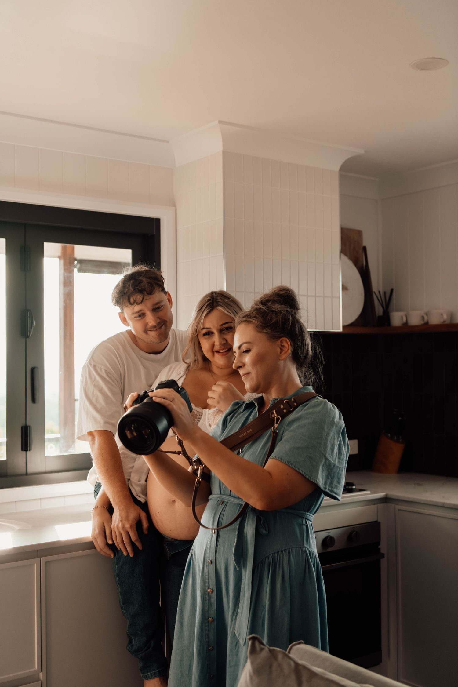 Three people gathered in a modern kitchen, smiling while reviewing photos on a camera together.