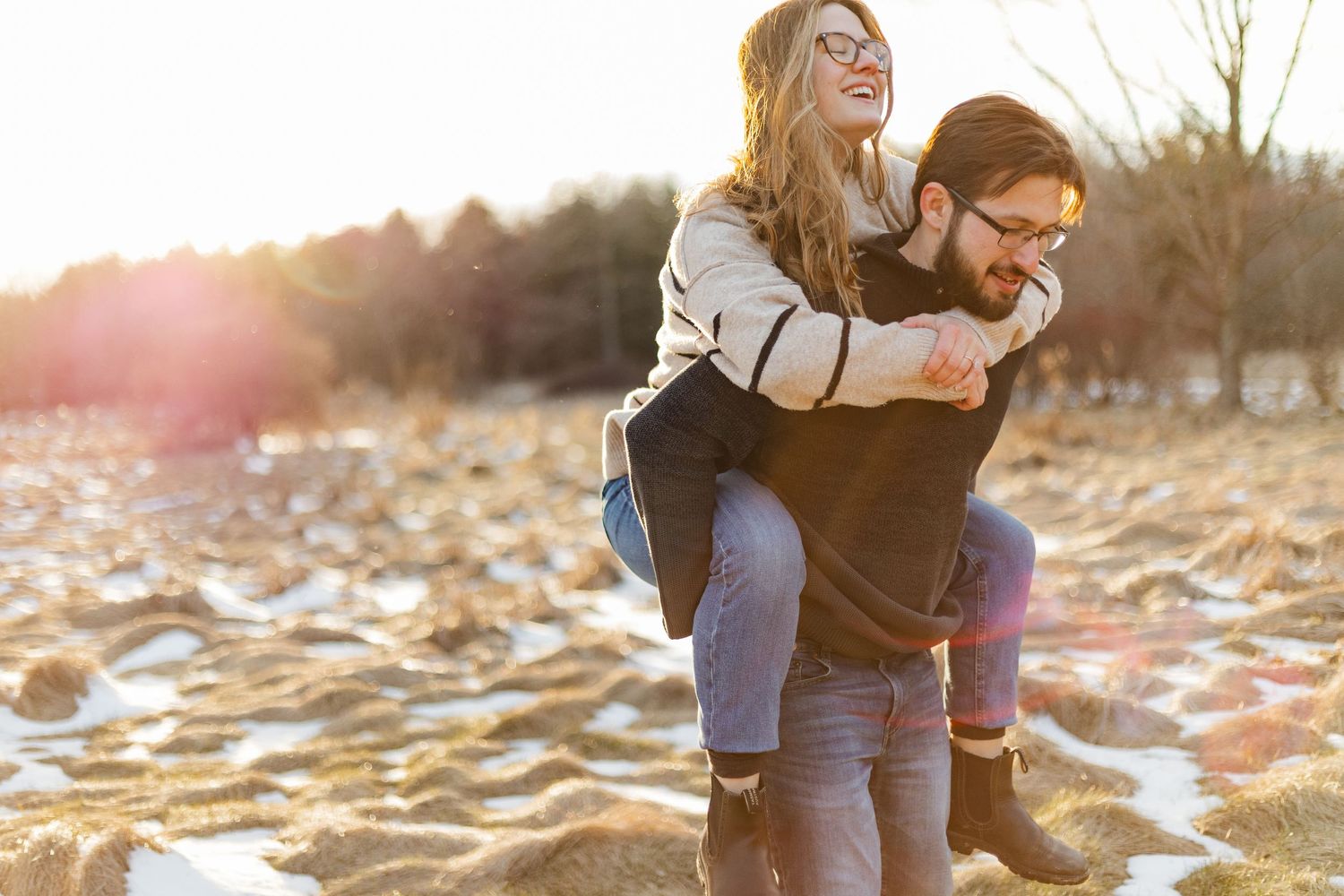 A couple in a piggy back in a field during their sunset engagement session at the guelph arboretum in guelph, ontario.