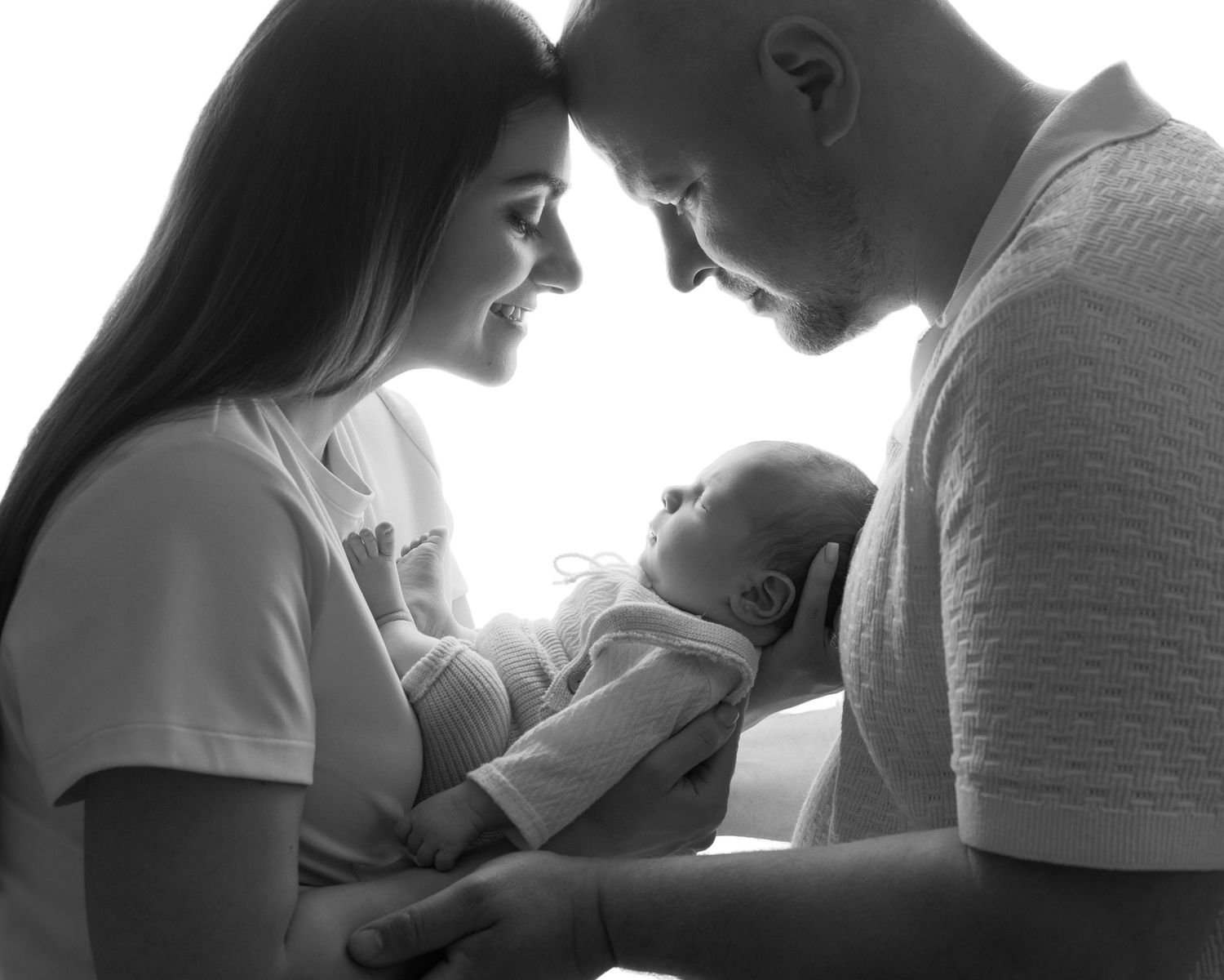Black and white photo of smiling parents gazing lovingly at their newborn baby held in mothers arms.