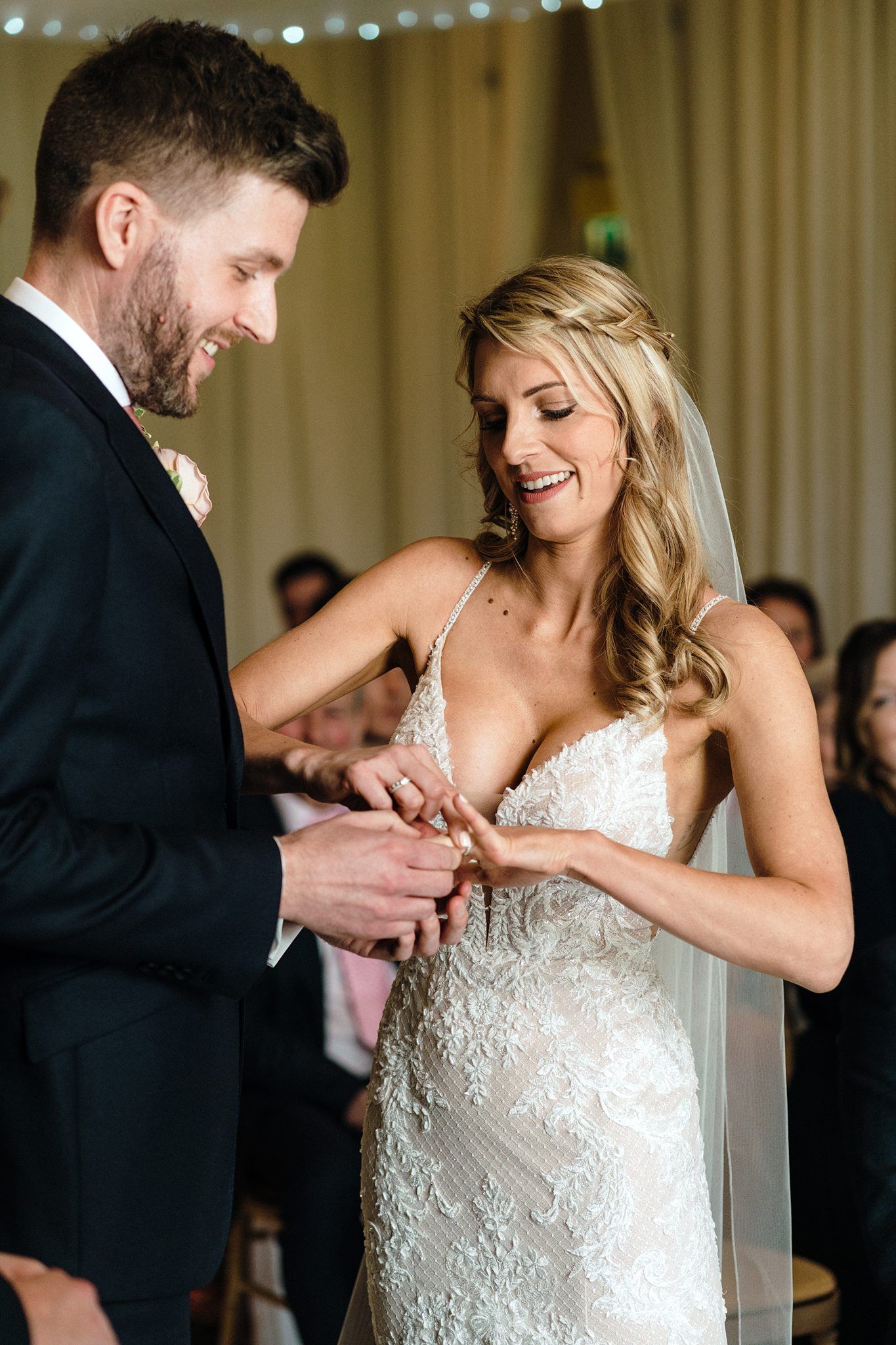 Bride and groom exchanging rings during wedding ceremony, bride wearing lace gown and veil, groom in black suit.