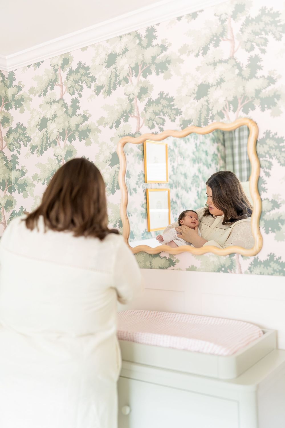 mom holding baby girl staring in from to mirror in nursery pink and green color, neutral tones
