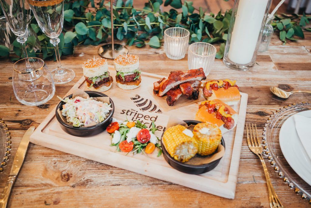 Striped Spatula catering board with sliders, ribs, salads, and stuffed potatoes on a rustic wooden table.