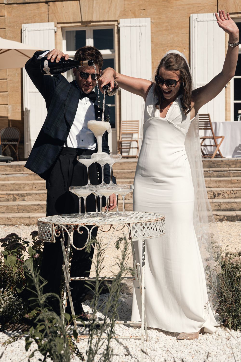 ritish bride and groom pouring champagne into a tower of coupe glasses during their wedding at Château de Sainte-Croix in the Dordogne