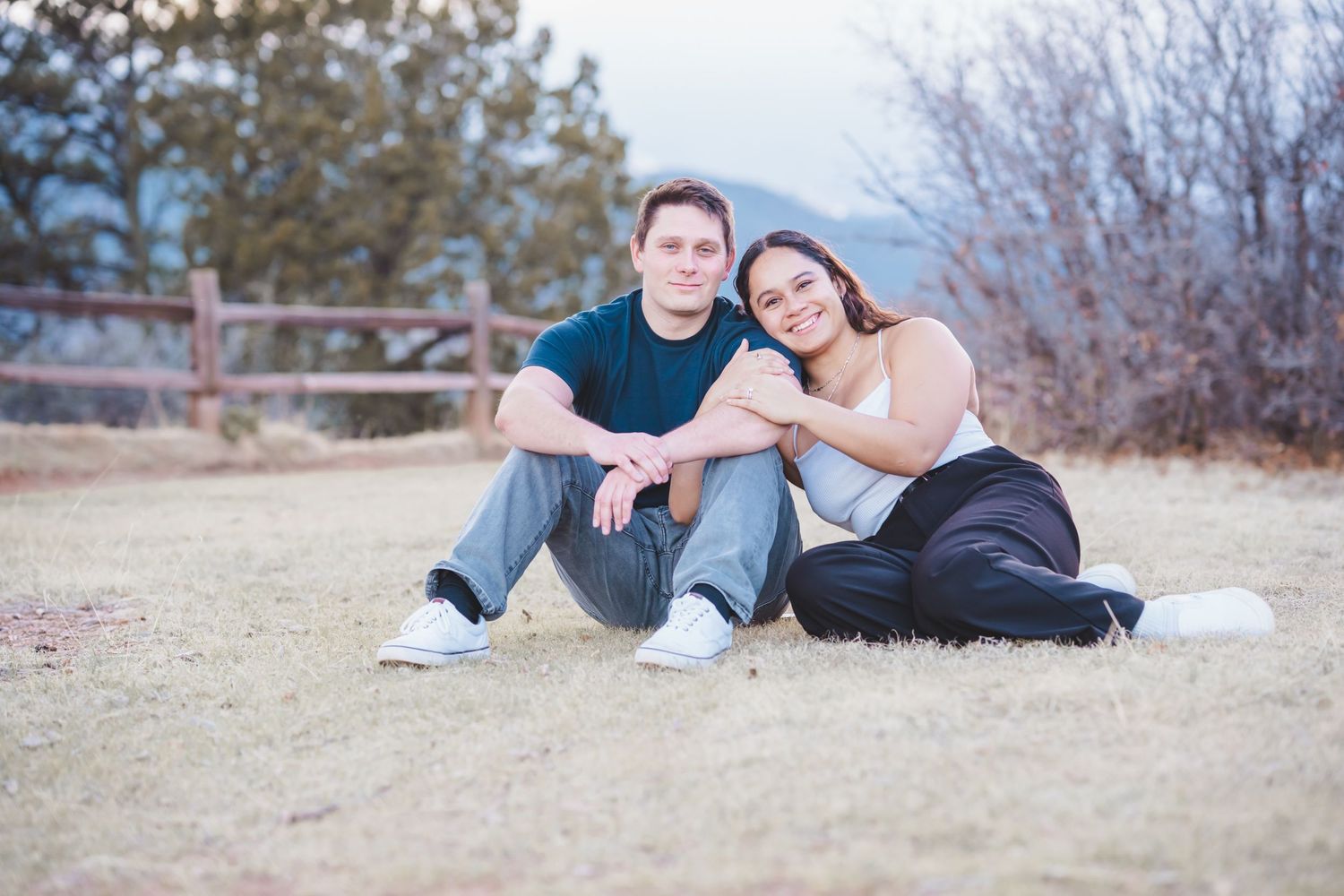 A couple sits casually together on dry grass during an outdoor photo session. engagement session garden of the gods colorado springs