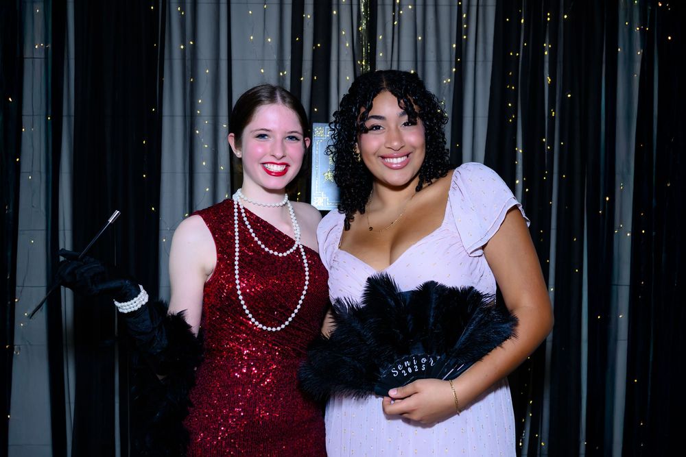 Two party guests pose together, one wearing a sparkly red dress with pearls and one in a white dress with black corset.