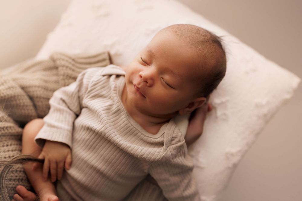 A peaceful sleeping baby wearing a knit sweater rests on a white pillow.