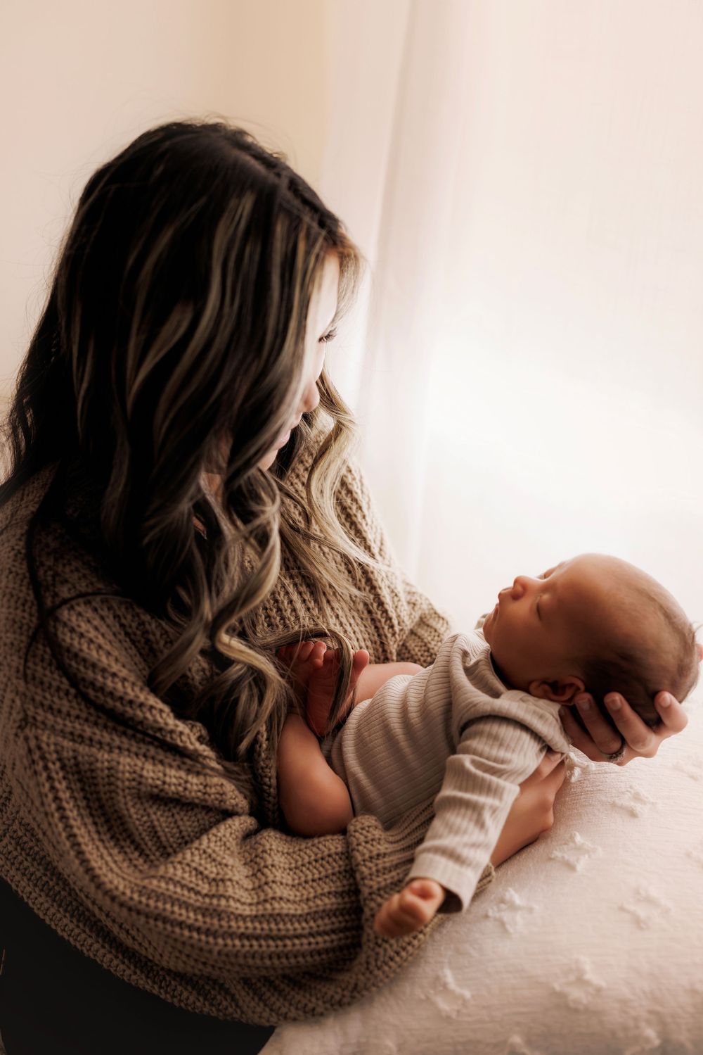 A parent in a cozy knit sweater cradles and gazes lovingly at their newborn baby in a tender moment.