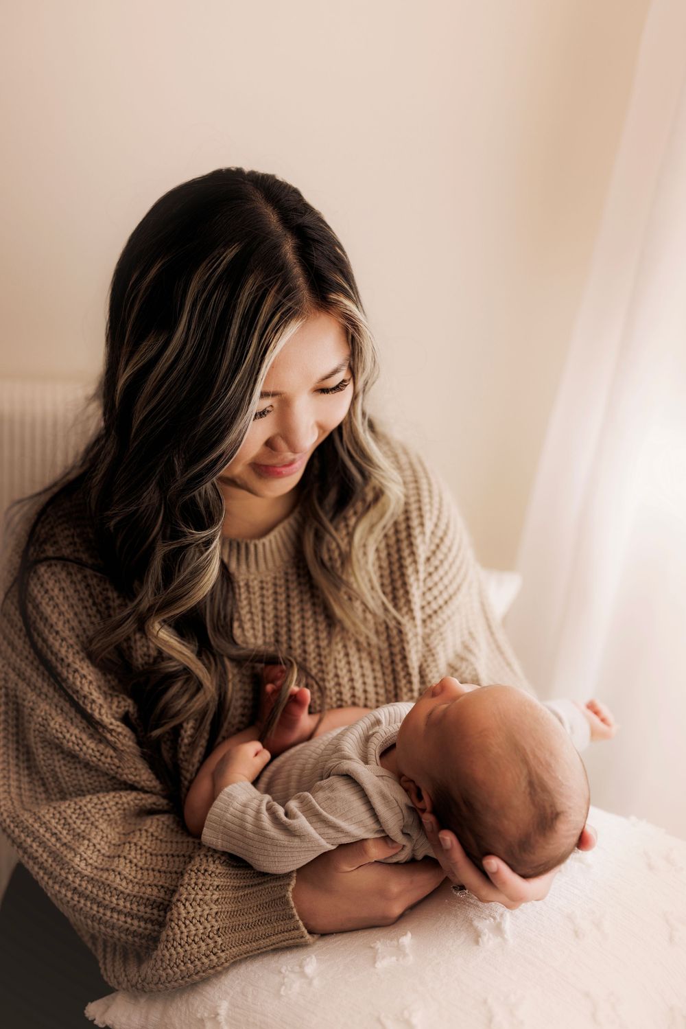 A tender moment between parent and newborn infant in soft natural light, wearing a cozy knit sweater.