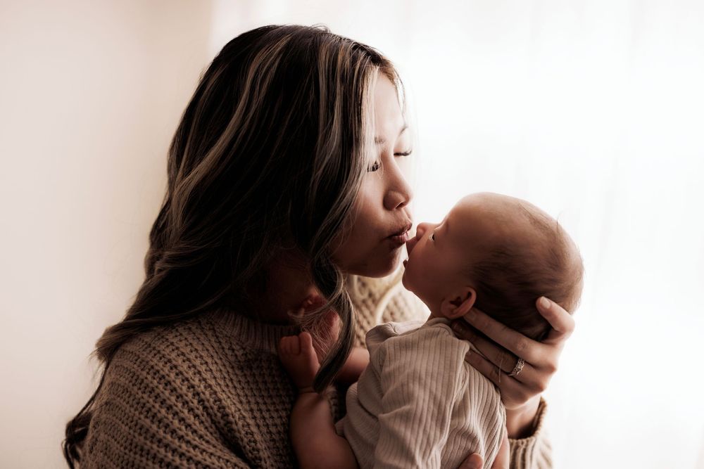 A tender moment between parent and baby in warm lighting as they share an affectionate moment by a white wall.