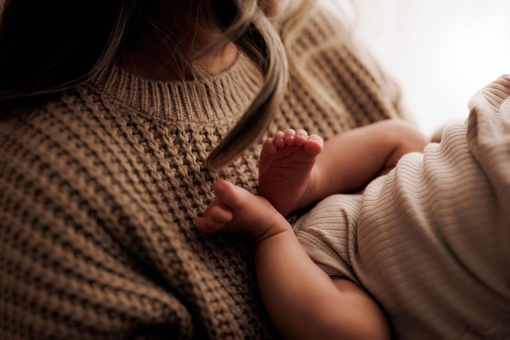 Tiny baby hand grasps a brown knit sweater in warm intimate lighting.
