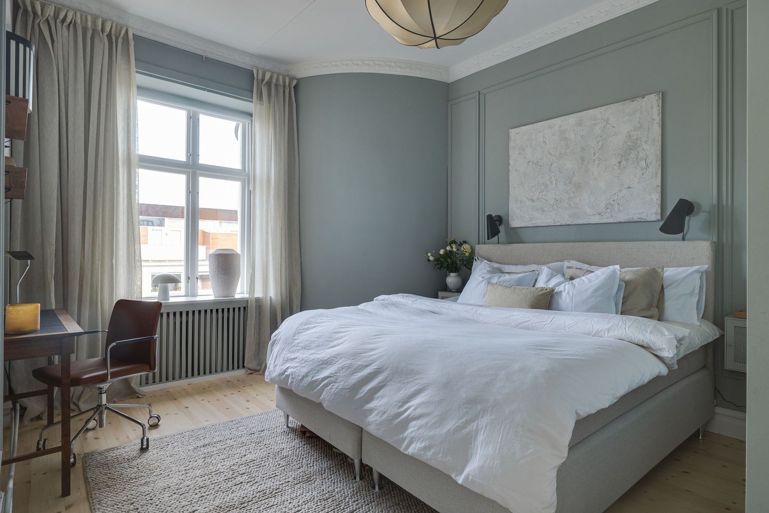 Serene bedroom with sage green walls, white bedding, natural light from large window, and modern pendant light fixture.