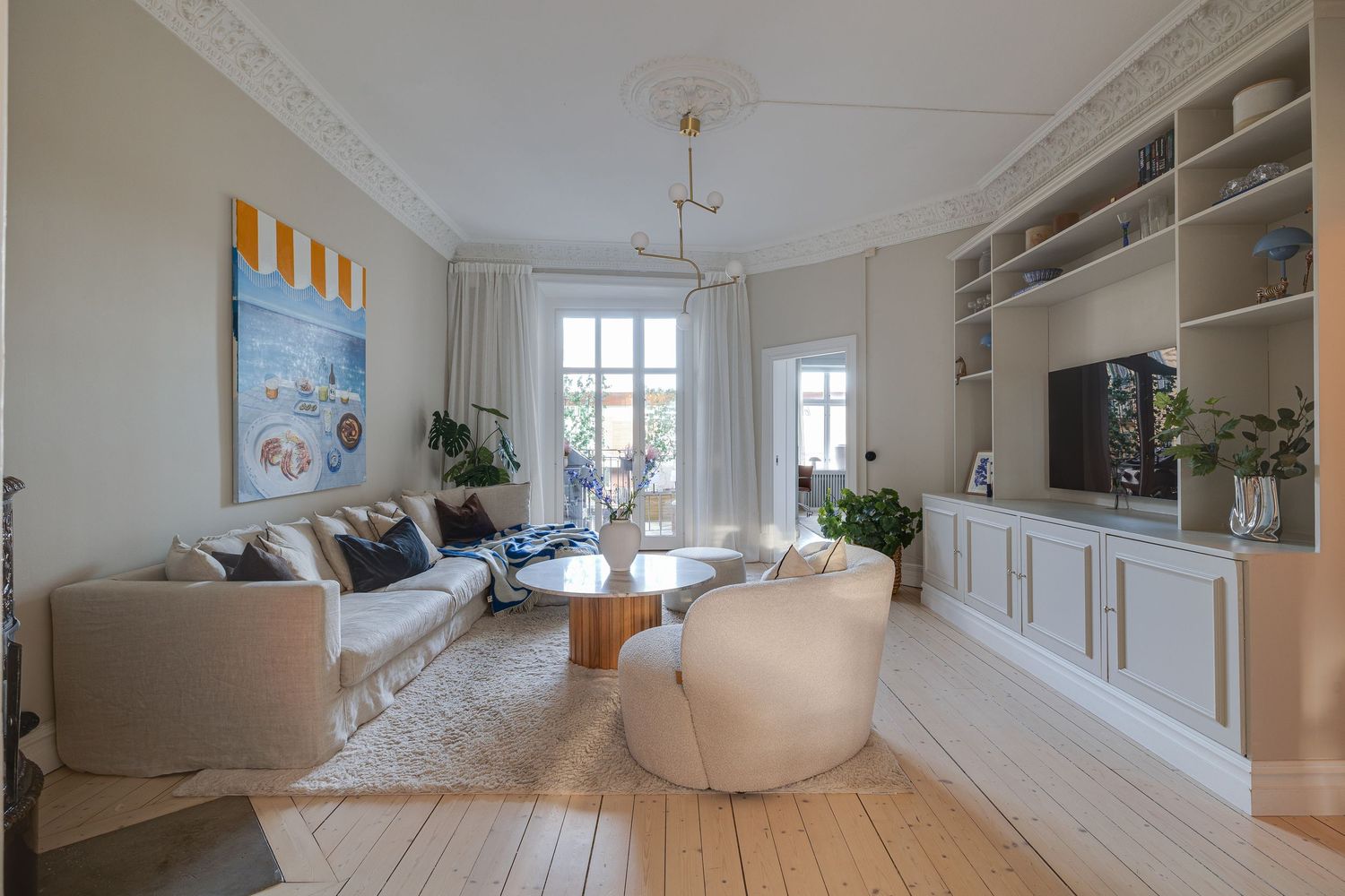 Modern Scandinavian living room with built-in shelving, light wood floors, crown molding and large windows letting in natural light.