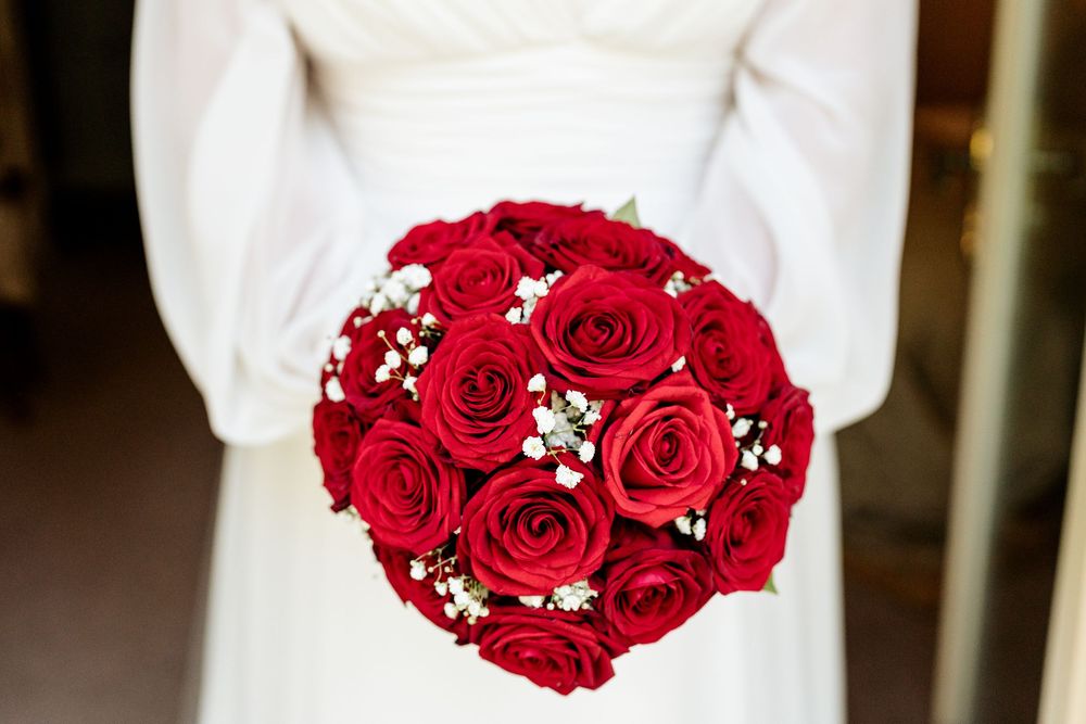 A classic round bridal bouquet of vibrant red roses accented with delicate white baby's breath flowers.