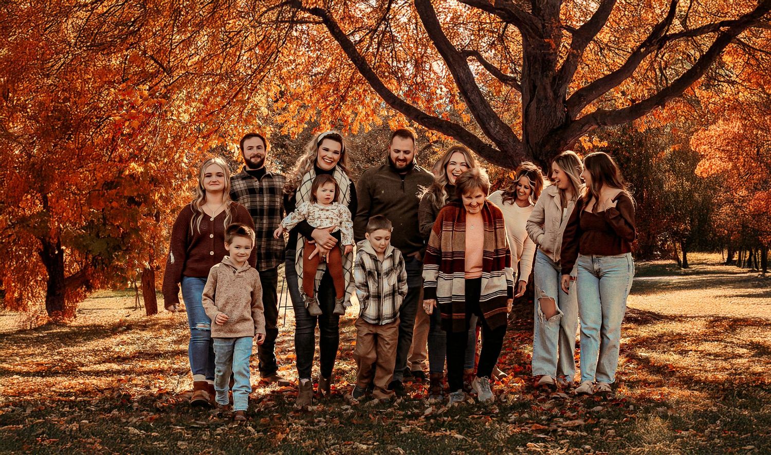 Family group posed beneath trees with brilliant orange autumn foliage.