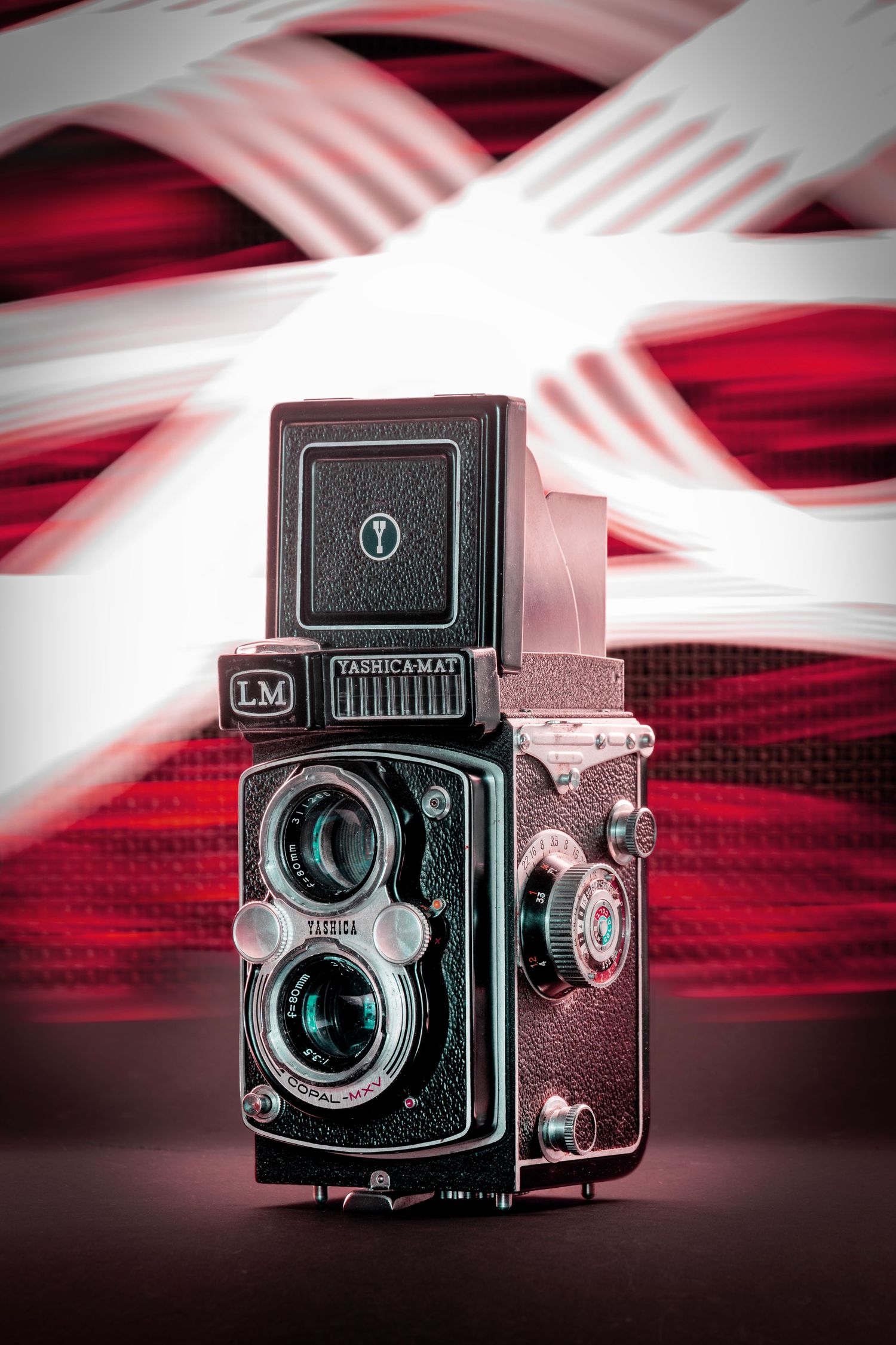 Vintage twin-lens reflex camera with metallic details, set against a red and white light-painted background.
