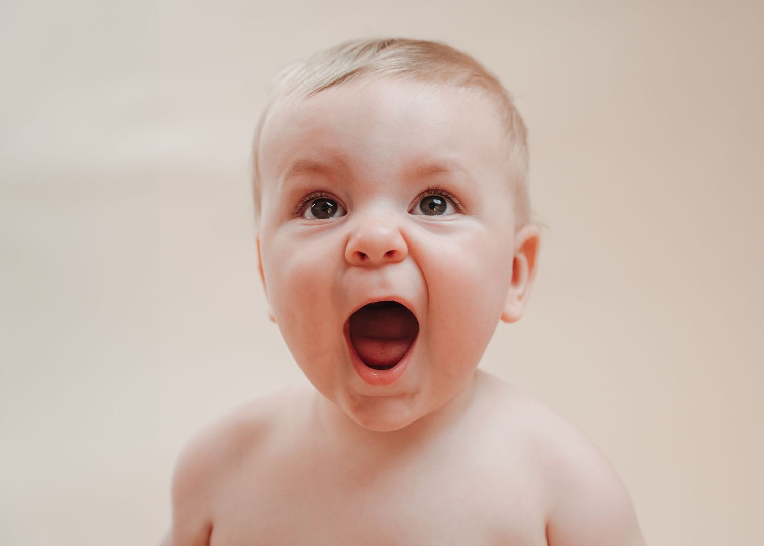 Baby with wide open mouth and excited expression against neutral background.